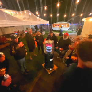 Woodsoak Wines garden with the Limoncello Caravan, a marquee and string lights. People are sitting and standing around an outdoor gas heater